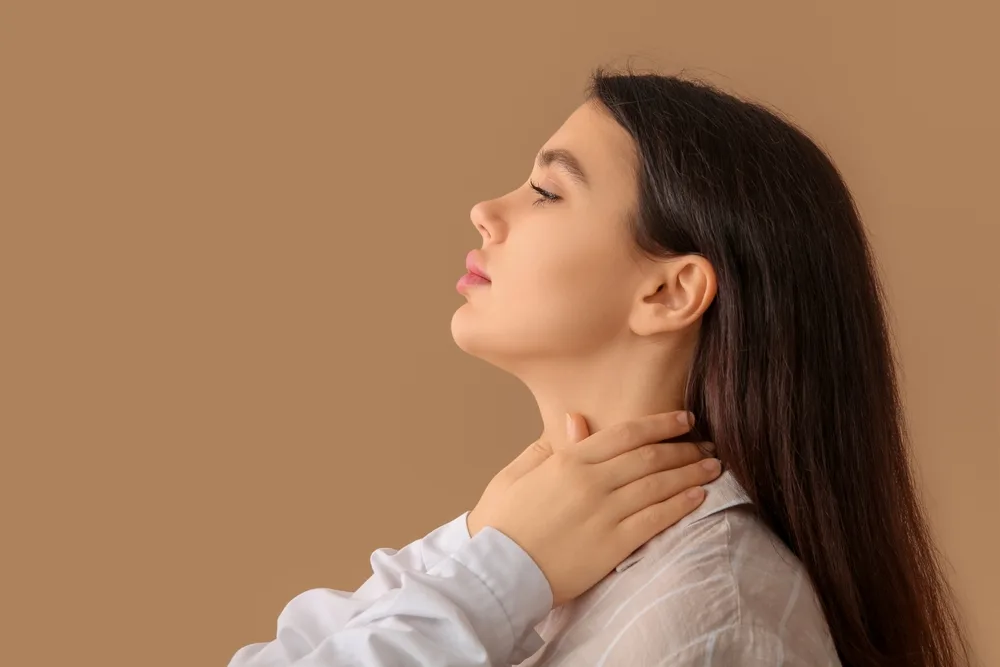 Woman touching her neck and throat area against a neutral background